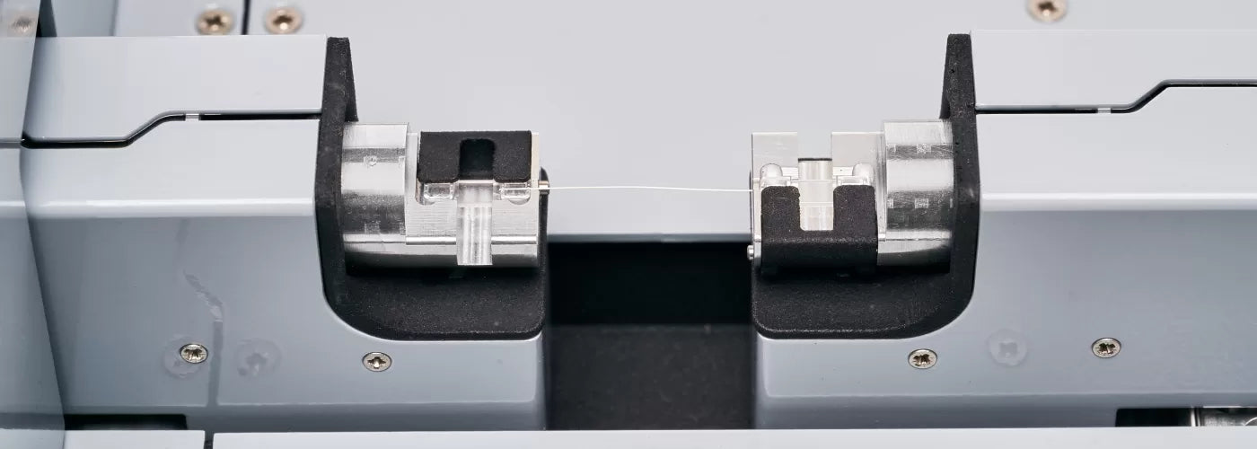 Close-up of a hair fiber stretched between precision laboratory clamps for tensile testing.